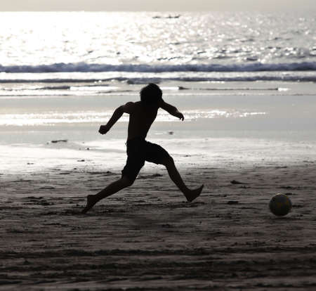 Young boy having fun on the beach playing footballの写真素材
