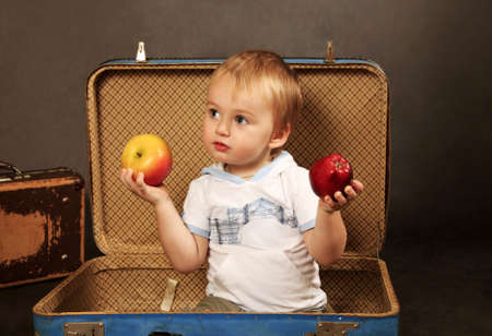 The little boy with a apples sits in a old suitcaseの写真素材