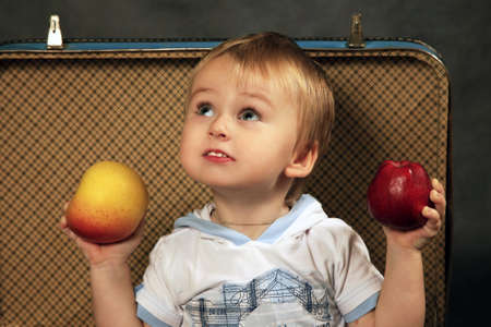 The little boy with a apples sits in a old suitcaseの写真素材