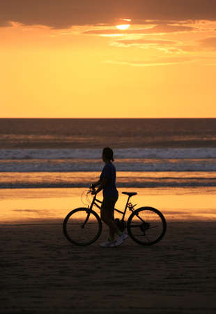 The woman with a bicycle on a coast of oceanの写真素材