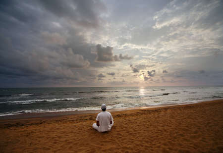 Guy meditating at sunset sitting on coastline の写真素材
