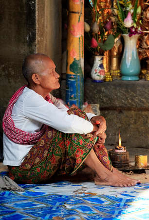 SIEM REAP, CAMBODIA - APRIL 06: Old wrinkled traditional Asian woman praying with incense sticks inside a temple in Siem Peap 06 April, 2014. Cambodiaのeditorial素材