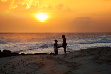 Red toned picture of a couple on a tropical beach at sunsetの写真素材