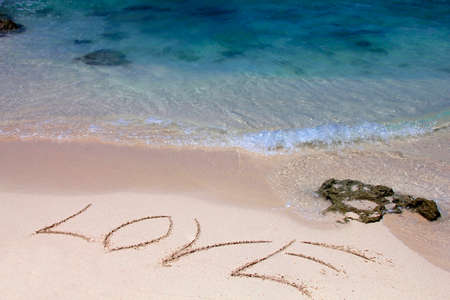 The word love is written by someone on sand