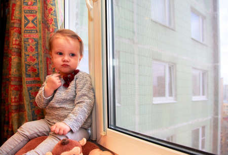 Sad little girl on a windowsill at homeの写真素材