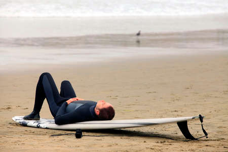 Surfer lying on a board resting on the beachの写真素材