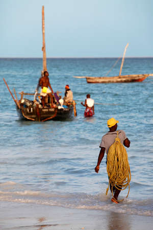 Stone Town Zanzibar, Tanzania - January 6, 2016: A dhow traditional sailboat in the background and a crowded fishing boat and fishman in the foreground in the Indian Ocean just off the island of Zanzibar, Nungwiのeditorial素材