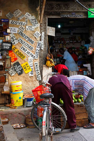 Stone town, Tanzania - December 30, 2015: Stone Town. Streets of the town are always lively. There are many shops, restaurants and bars, where tourists can relax and buy suvenirs. Here is a man apparently collecting old number plates.のeditorial素材