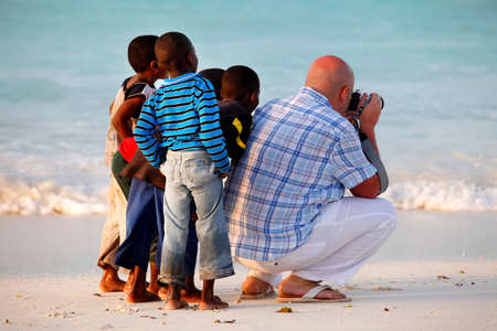 Nungwi, Zanzibar, Tanzania - January 9, 2016:  Large white man-tourist with African children on beach of village Nungwi. Zanzibar, Tanzaniaのeditorial素材