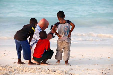 Nungwi, Zanzibar, Tanzania - January 9, 2016:  Large white man-tourist with African children on beach of village Nungwi. Zanzibar, Tanzaniaのeditorial素材