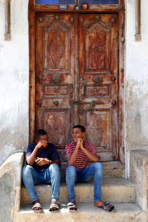 Stone Town, Zanzibar, Tanzania - January 1, 2016: two young men sit on the steps in the background a traditional wooden door in Stone Town, Zanzibarのeditorial素材