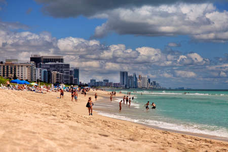 Miami Beach, USA - May 5, 2013: Scene of the crowded beach. People having fun, sunbathing and swimming in the shallow water. Skyline in the back.のeditorial素材