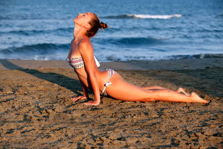Young woman practicing yoga on the sea beach at sunsetの写真素材