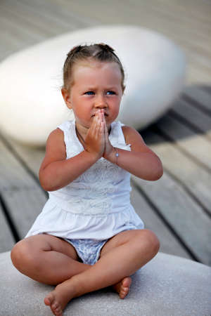 Adorable little girl doing yoga sitting on the big stoneの写真素材