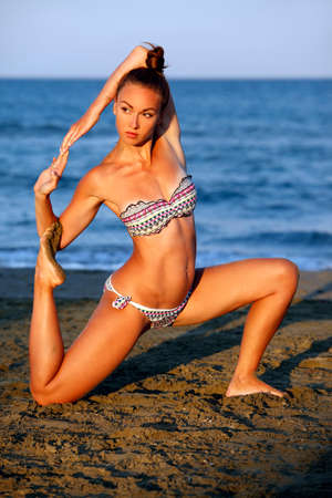 Young woman practicing yoga on the sea beach at sunsetの写真素材