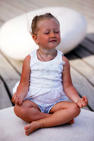 Adorable little girl doing yoga sitting on the big stoneの写真素材