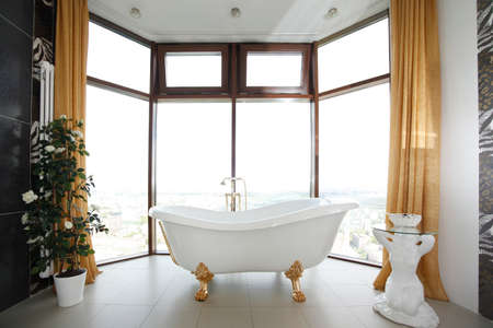 White tub on gold legs in front of large windowsの写真素材