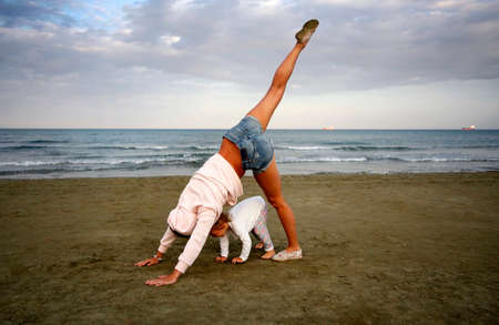 Young woman with small douther practicing yoga on the sea beach at sunsetの写真素材