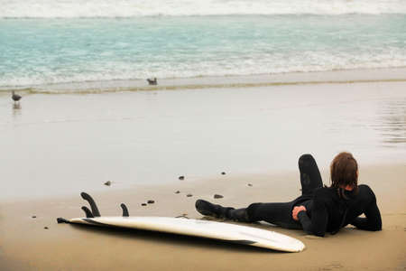 Surfer lying on a board resting on the beachの写真素材
