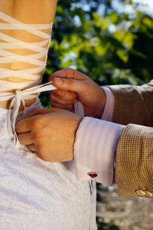 The groom helps the bride to tie a ribbon on the dressの写真素材