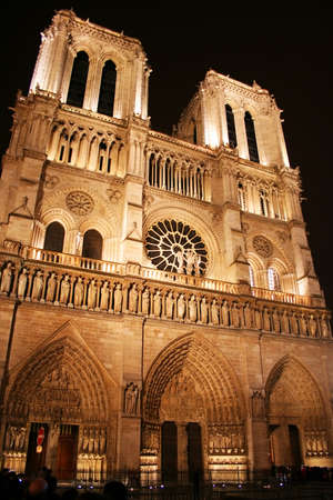 Paris, France - December 25, 2005: Evening in Paris, and the lights on Paris's iconic Cathederale de Notre Dame come on, illuminating the grand structure's gothic features. Numerous tourists are blurred by the long exposure.の写真素材