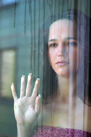Woman with sad smile behind a wet windowの写真素材