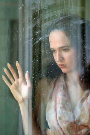 Woman with sad smile behind a wet windowの写真素材