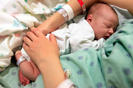Sleeping newborn baby in the arms of my mother in hospitalの写真素材