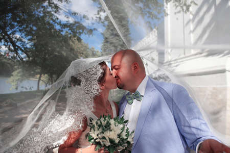 The groom and the bride kiss having closed by a veilの写真素材