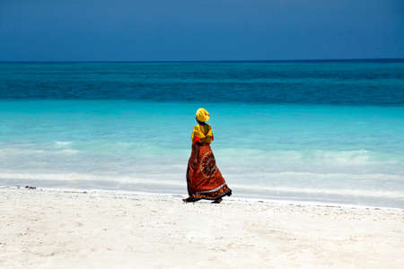 Zanzibar, Tanzania - January 7, 2016: An African woman in traditional dress walks down the beach. Zanzibar, Tanzaniaのeditorial素材