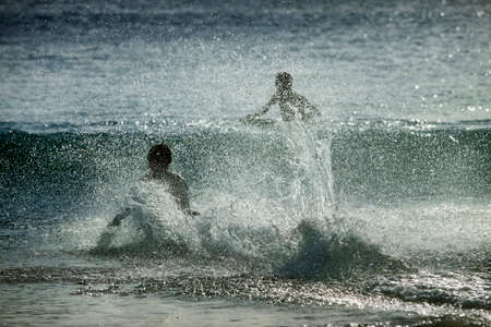 Silhouettes of people in the splashes of the ocean at sunset