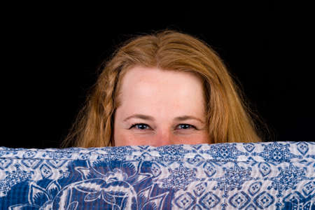 Portrait of a attractive european light overweighted red haired female, hiding behind a blue-white scarf, headshot, studioshot in front of black backgroundの写真素材