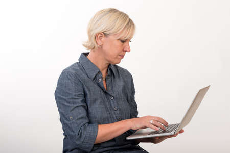 beautiful european mid aged woman working at a laptop - studio shot in front of light background