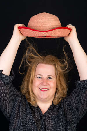 Portrait of attractive european light overweighted woman lifting her hat in front of dark backgroundの写真素材