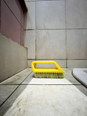 Cleaning the tile floor with a yellow broom in the bathroom.