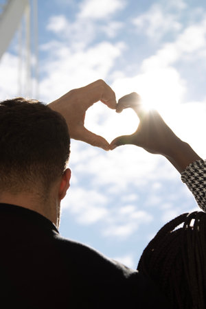 Young couple making a heart shape with their hands against the blue sky