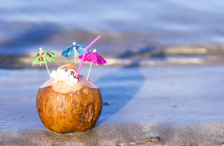 Coconut with drinking straw, umbrellas and flowers, on sand at the sea in protaras, cyprus islandの写真素材