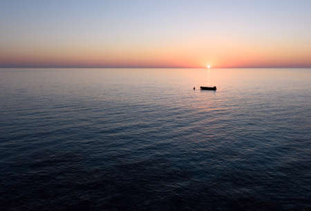 Sunrise with reflection of light in the water, in protaras paralimni, a fishing boat, dark blue sea and rocks, cyprus islandの写真素材