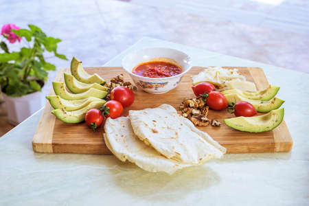Wood plate with food, on a white table. Tomato, avocado, wallnuts and parmesan cheese with pita breadの写真素材
