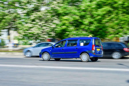 Car rides on city road with ghost effect. Buildings, green trees and parked cars on background.