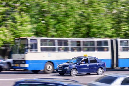 Bus rides on city road with ghost effect. Buildings, green trees and parked cars on background.の写真素材
