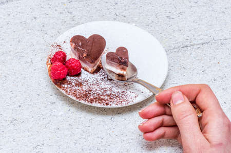 Valentines day desserts. Heart shaped chocolate cake slices on white plates with raspberry fruit decorations. Bright table.の写真素材