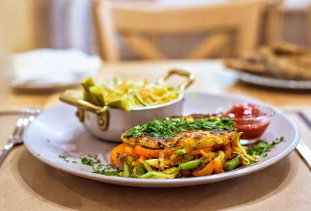 Potatoes and grilled vegetables with cucumbers and cabbage salad on a white plate in a restaurantの写真素材