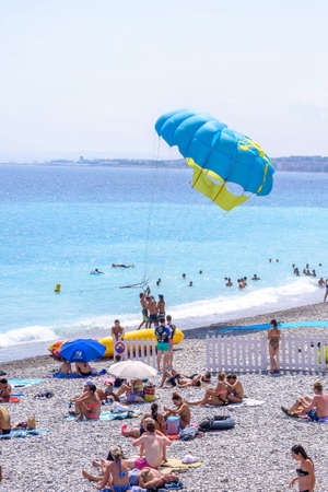 NICE COTE D'AZUR, FRANCE - JUNE 27,2017: Beautiful daylight view to a parachute man preparing for takeoff. People walking on beach.のeditorial素材