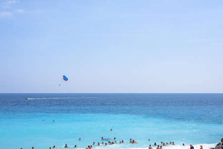 NICE COTE D'AZUR, FRANCE - JUNE 27,2017: Beautiful daylight view to beach resort. Blue water with people walking on sand and parachute man cruising in air.のeditorial素材