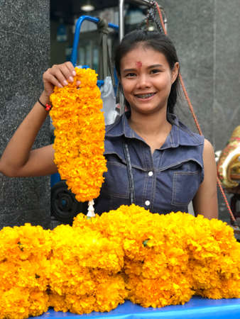 BANGKOK, THAILAND - SEPTEMBER 30, 2017: Smiling asian brown hair woman holding in hand yellow flowers bouquet for sale in the streetsのeditorial素材