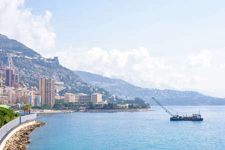 Daylight sunny view to city buildings and beach. Ship cruising on water. Big green mountains and bright blue sky on background. Monaco, Franceの写真素材
