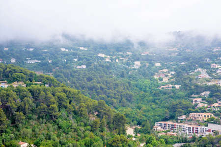 Daylight foggy view to Eze village, trees and clouds above mountains from castle. Old houses and roads of a French Rivieraの写真素材