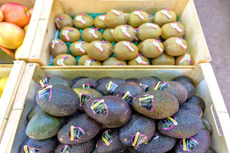 BEAULIEU-SUR-MER, FRANCE - JUNE 28, 2017: Avocado sublime gold, apples and kiwi with stickers in wood boxes for sale in local marketplace.のeditorial素材