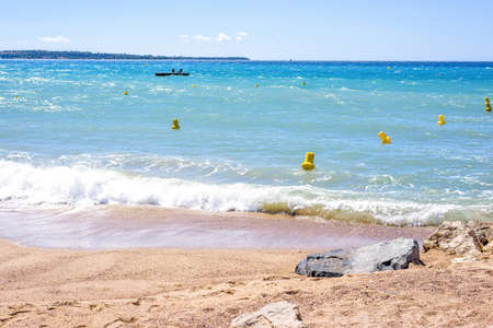 Daylight view from rocks to blue sea and bright clear sky. Yellow buoys and a platform with people on water. Trees on background. Cannes, Franceの写真素材